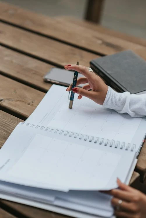 crop-ethnic-businesswoman-with-open-notepad-at-table